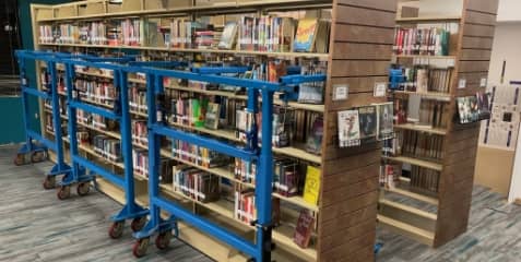 Library stacks filled with books with gray patterned flooring with specialized blue moving equipment for the stacks.