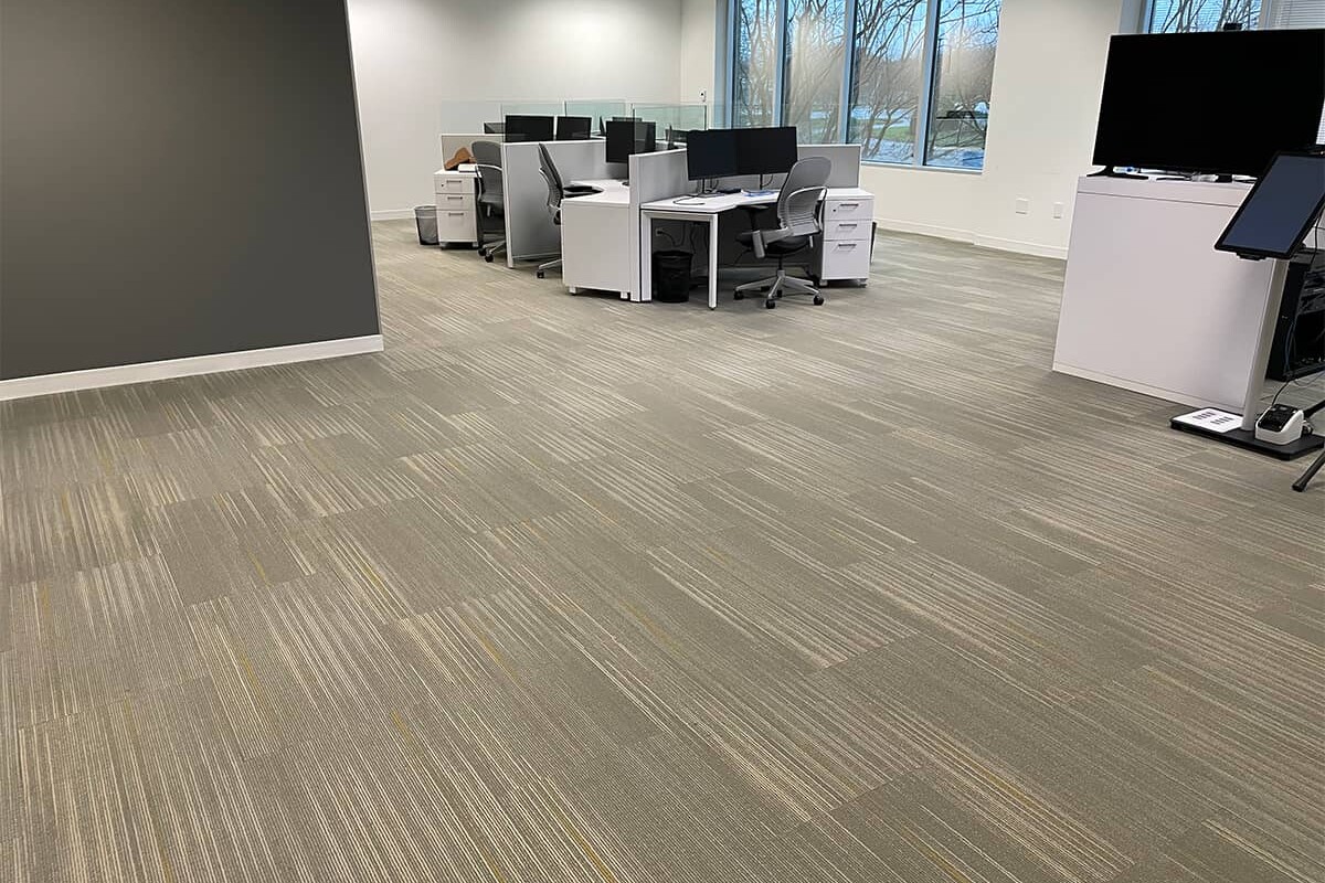Office with gray walls and cubicles with beige commercial flooring.