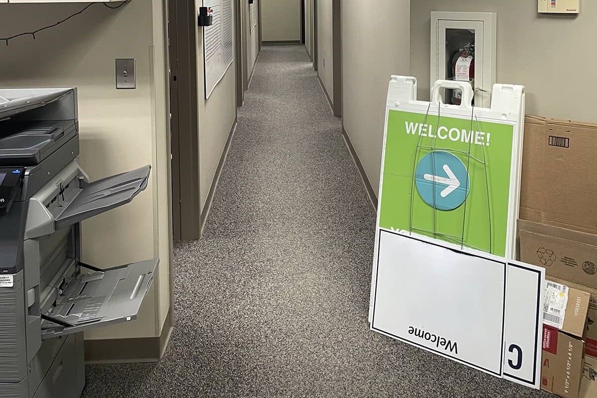 Office hallway showing gray carpet with a copier and signs leaning against a wall.