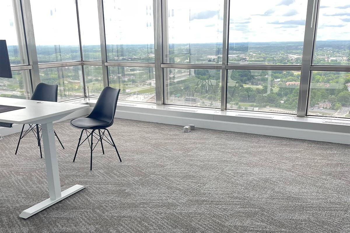 Large office with glass windows and new gray carpet with white desk and black chairs.