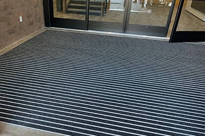 Walk off mat in front of a glass door at entrance of a commercial building.